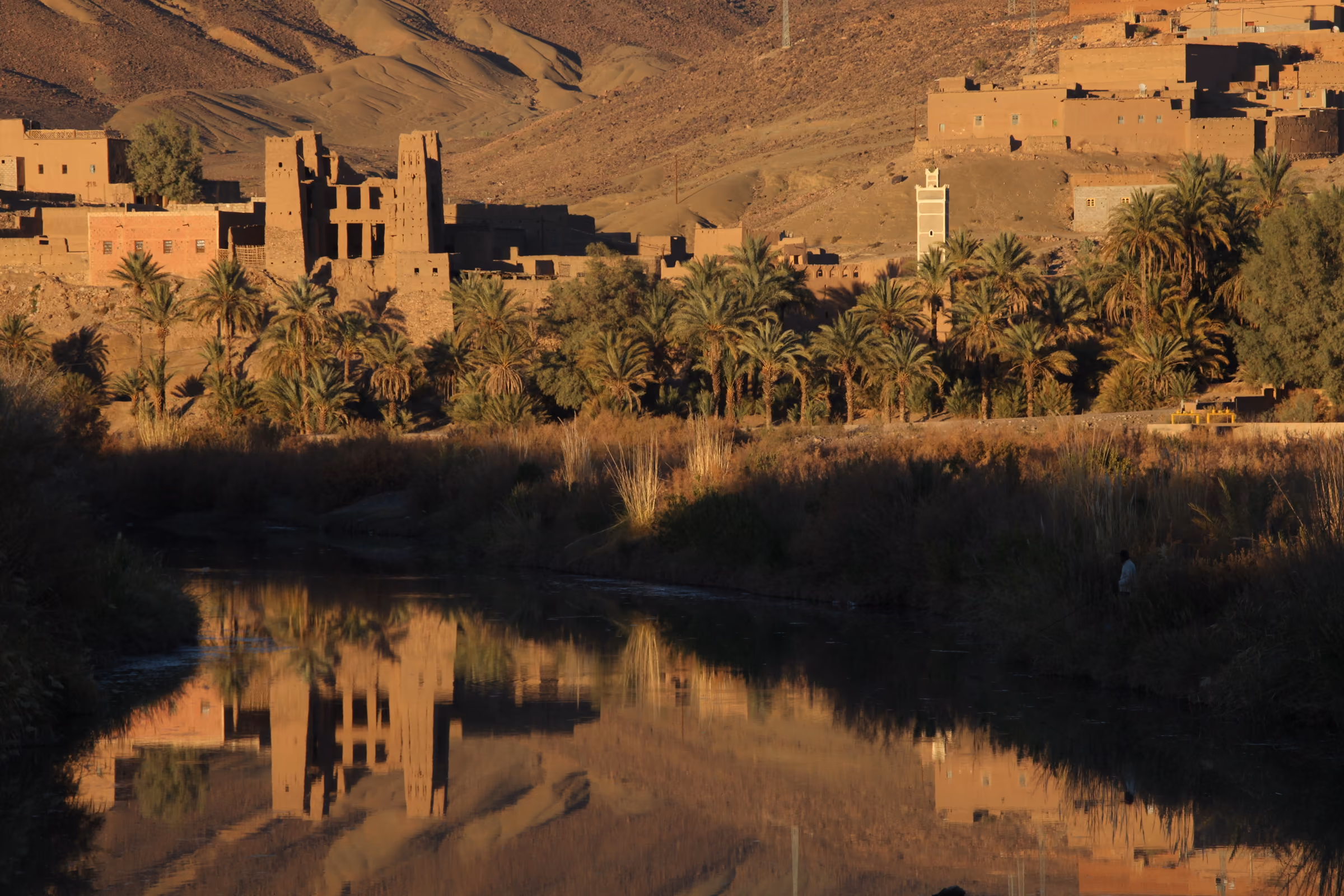 Kasbahs de adobe y palmeral reflejados en el río Draa camino de Zagora